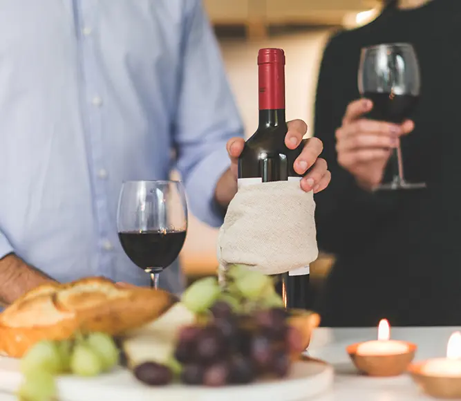 A person holding a wine bottle near some grapes.